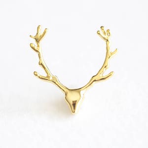 May include: A gold-colored, antler-shaped decorative object. The antlers are detailed with multiple points and curve upwards. The object has a smooth, polished finish and is set against a white background.