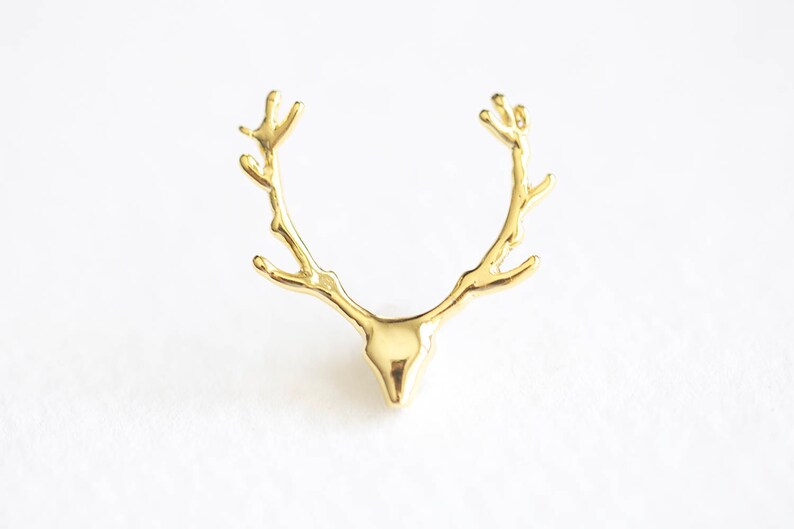 May include: A gold-colored, antler-shaped decorative object. The antlers are detailed with multiple points and curve upwards. The object has a smooth, polished finish and is set against a white background.