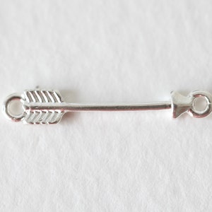 May include: Silver arrow charm with a loop on each end. The arrow is detailed with lines and a pointed tip.
