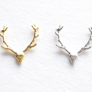 May include: Two metal deer antler pendants, one gold-toned and one silver-toned, are displayed against a white background. The pendants are detailed with a textured finish, showcasing the shape of a deer's antlers.