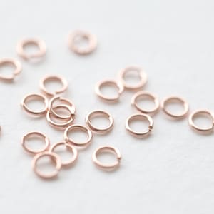 May include: A collection of rose gold jump rings, a type of jewelry finding used for connecting chains, cords, and other jewelry components.