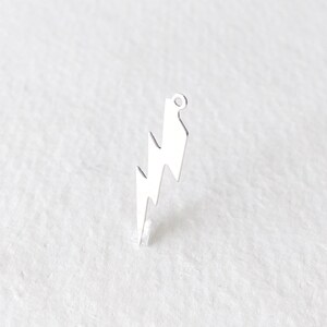 May include: A silver-colored lightning bolt charm with a small loop at the top for attaching to jewelry. The charm has a jagged zig-zag design and is set against a white background.