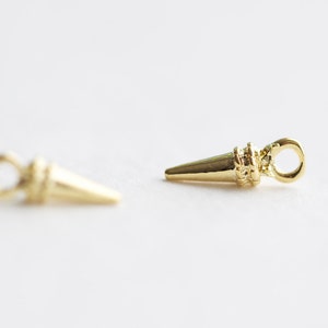 May include: Two gold-toned metal cone-shaped charms with a loop at the top. The charms are about 1 inch long.