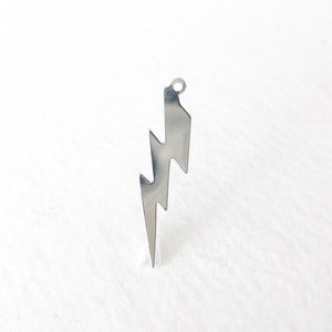 May include: A silver-colored lightning bolt pendant with a small loop at the top for hanging. The pendant has a jagged, zig-zag design, and is displayed against a white background. This jewelry item is suitable for necklaces or earrings.