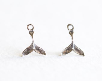 Op de afbeelding: Twee zilverkleurige zeemeerminstaartbedels. Elke bedel heeft een gedetailleerd staartontwerp met een lus aan de bovenkant om aan sieraden te bevestigen. De bedels worden tegen een witte achtergrond getoond.