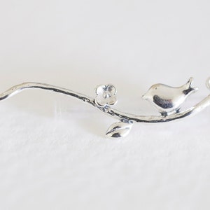 Peut inclure: Breloque en argent représentant un oiseau perché sur une branche avec une fleur. Le breloque a une boucle à chaque extrémité pour l'attacher à un bracelet ou un collier.