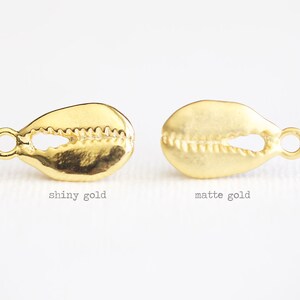 May include: Two gold cowrie shell charms, one with a shiny finish and the other with a matte finish.
