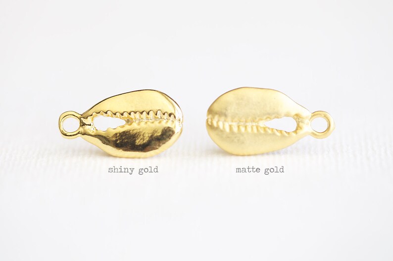 May include: Two gold cowrie shell charms, one with a shiny finish and the other with a matte finish.