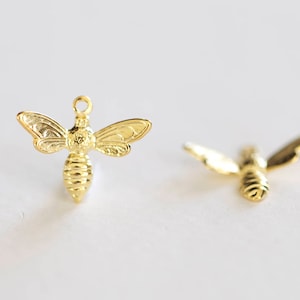 Puede incluir: Dos abalorios de abeja de oro con alas detalladas y un cuerpo texturizado. Los abalorios de abeja son perfectos para la elaboración de joyas o manualidades.