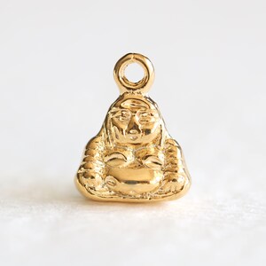 May include: Gold-coloured charm of a sitting Buddha figurine with a loop for attaching to a necklace or bracelet.