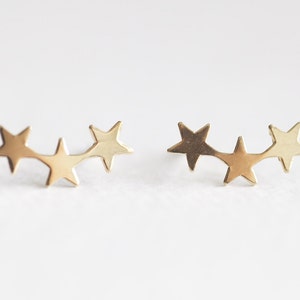 May include: A pair of gold star earrings, each featuring three connected stars in a curved line.