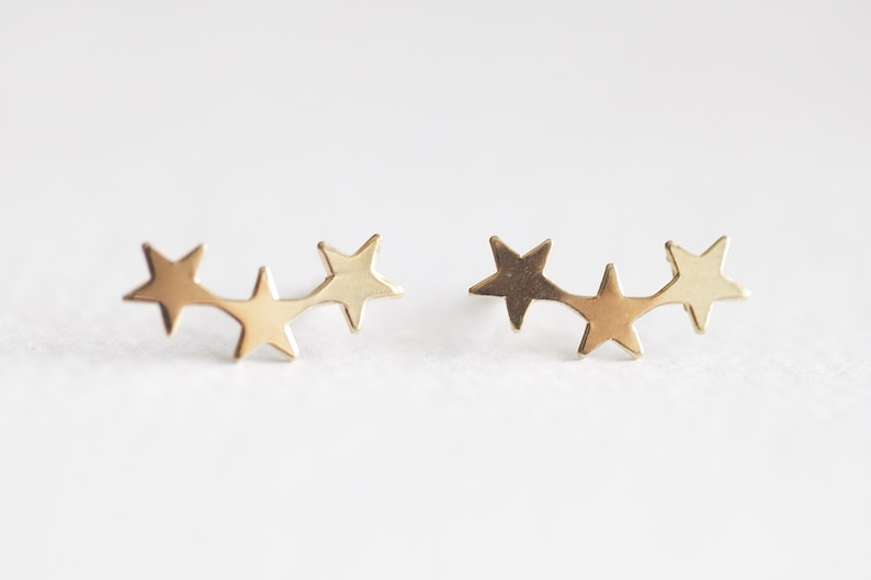 May include: A pair of gold star earrings, each featuring three connected stars in a curved line.