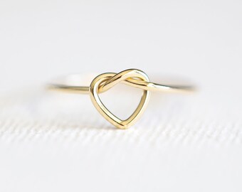 May include: A gold heart-shaped ring with a knot design.