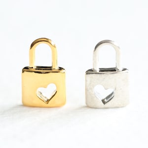 May include: Two small lock charms, one gold and one silver, with a heart-shaped cutout in the front.
