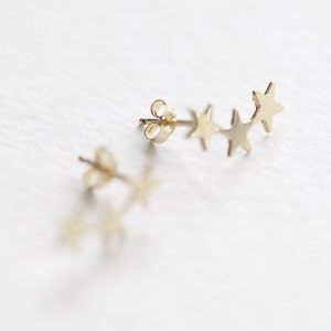 May include: A pair of gold star earrings. Each earring features a row of five small, star-shaped charms.