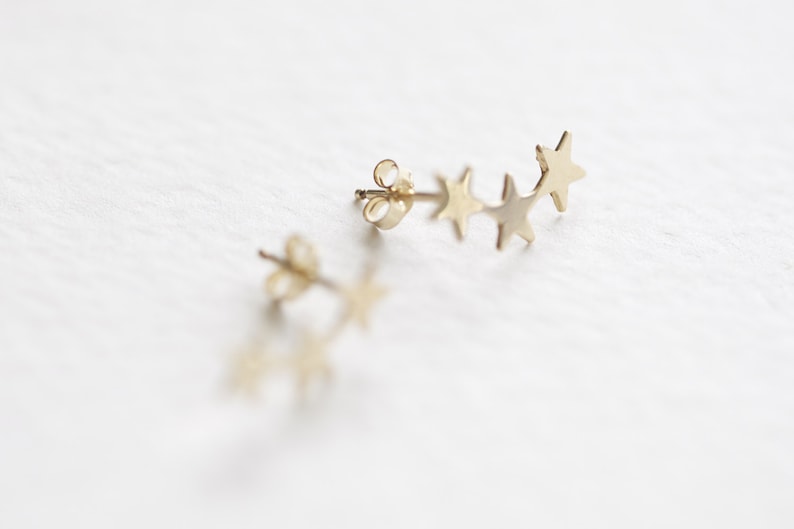 May include: A pair of gold star earrings. Each earring features a row of five small, star-shaped charms.