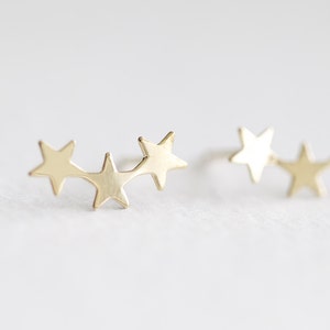 May include: A pair of gold star earrings. Each earring features three connected star shapes.