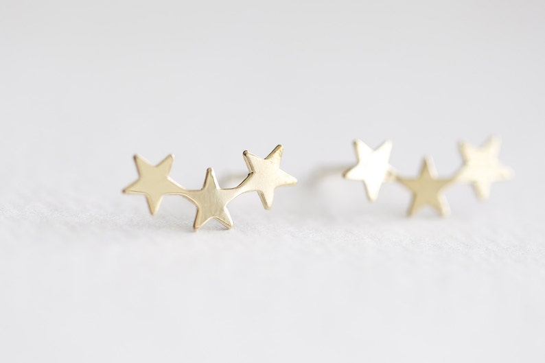May include: A pair of gold star earrings. Each earring features three connected star shapes.