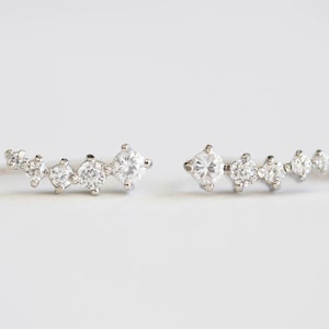 May include: A pair of silver earrings with a curved row of small, clear cubic zirconia stones.