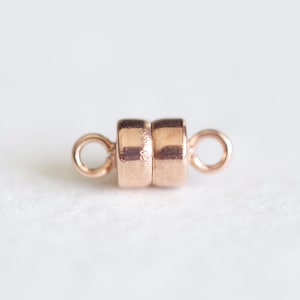 May include: A rose gold magnetic clasp for jewelry making. The clasp is made of two round pieces with a small loop on each side.