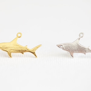 May include: Two shark charms, one gold and one silver, with a loop at the top for attaching to jewellery.