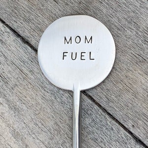 May include: A silver metal stirring spoon with a round handle that says "MOM FUEL" in all caps.