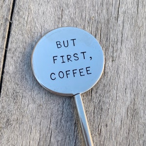 May include: A silver metal stirring spoon with a round handle that says "BUT FIRST, COFFEE".