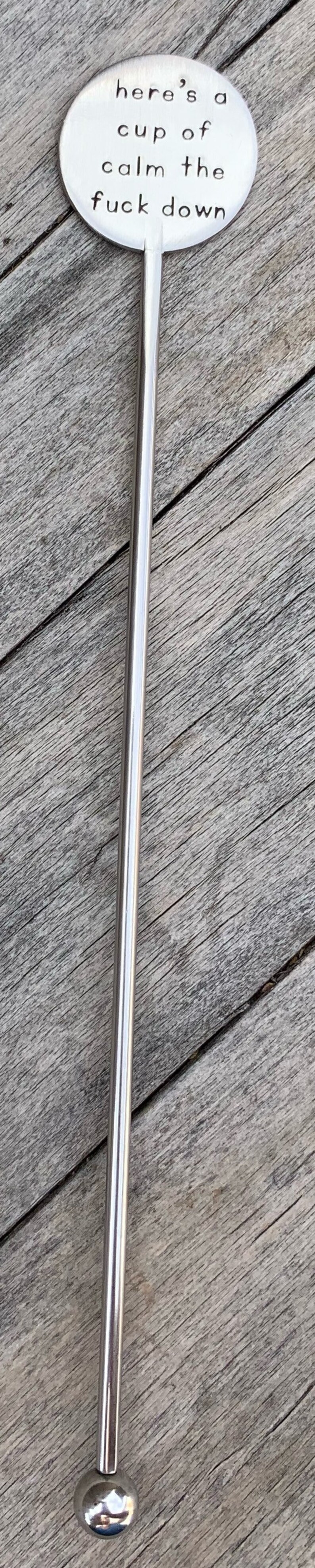 K&ouml;nnte beinhalten: Ein silberner R&uuml;hrl&ouml;ffel mit einem runden, flachen Ende, auf dem "here's a cup of calm the fuck down" steht.