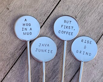 May include: Four silver metal stirring sticks with round metal discs attached to the top. The discs have different sayings on them: "A hug in a mug", "But first, coffee", "Java Junkie", and "Rise & Grind".