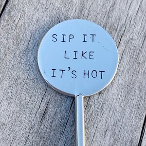 May include: A silver metal stir stick with a round, flat top that says "Sip it like it's hot".