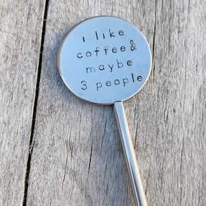 May include: A silver metal stirring stick with a round, engraved head that reads "I like coffee & maybe 3 people".