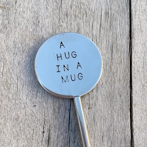 May include: A silver metal stirring spoon with a round, flat end that says "A HUG IN A MUG".