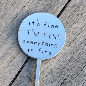 May include: A silver metal stirring spoon with a round handle that says "It's fine I'M FINE everything is fine" on it.