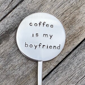 May include: A silver metal spoon with a round, flat handle that says "coffee is my boyfriend".