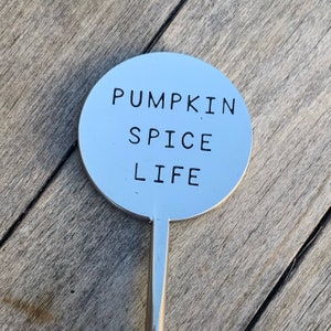 May include: A silver metal stick with a round, flat top. The top has the words "Pumpkin Spice Life" engraved on it.
