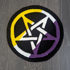 May include: A round rug with a black background and a white five-pointed star in the center. The star is surrounded by a yellow, white, and purple ring.
