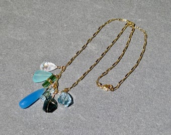 Puede incluir: Un collar dorado con una variedad de colgantes de piedras preciosas de colores. Los colgantes incluyen piedras azules, verdes y transparentes de varias formas. El collar tiene una cadena delicada y un cierre.