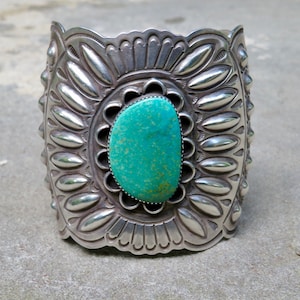 May include: A silver cuff bracelet with a turquoise stone set in the center. The bracelet is decorated with intricate designs and patterns.
