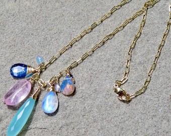 Puede incluir: Un collar de cadena dorada con un dije que presenta una variedad de piedras preciosas, incluyendo azul, rosa y blanco.