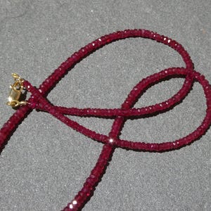 May include: A deep red gemstone necklace with a gold clasp. The necklace is made of small, faceted beads, creating a sparkling effect. The beads are strung together to form a delicate, elegant piece of jewelry.