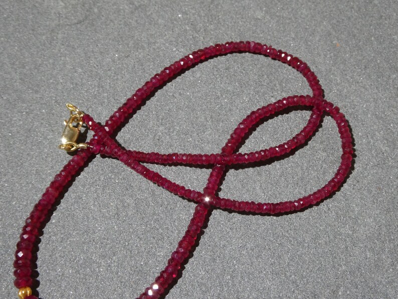 May include: A deep red gemstone necklace with a gold clasp. The necklace is made of small, faceted beads, creating a sparkling effect. The beads are strung together to form a delicate, elegant piece of jewelry.