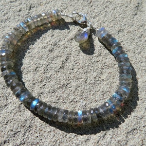 Puede incluir: Un brazalete de plata con un dije de piedra labradorita. El brazalete está hecho de cuentas de labradorita facetadas y tiene un cierre de plata.