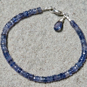 May include: A silver bracelet with a blue gemstone charm. The bracelet is made of small, faceted blue gemstones and has a silver clasp.