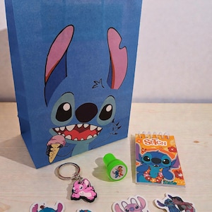 May include: A blue paper gift bag featuring a cartoon character eating ice cream. The image also shows a keychain, stickers, a stamp, and a notepad, all with the same cartoon character theme. The items are arranged on a light-colored surface.