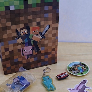 May include: A selection of Minecraft-themed merchandise, featuring a gift bag with pixelated characters, stickers, keyrings, and a TNT block. The items are displayed on a light surface, highlighting the game's distinctive blocky design.