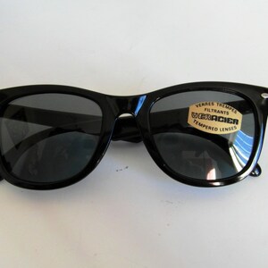 May include: Black plastic sunglasses with a gold label that reads "Verres Trempes Filtrants Ultracier Tempered Lenses".