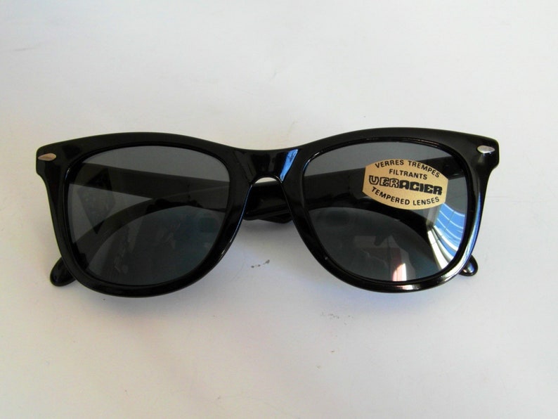 May include: Black plastic sunglasses with a gold label that reads "Verres Trempes Filtrants Ultracier Tempered Lenses".