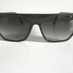 May include: Black sunglasses with a brown and black marbled frame. The lenses are dark and have a slight gradient.