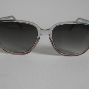 May include: Clear plastic sunglasses with a dark grey gradient lens. The frame has a pink and blue tint.