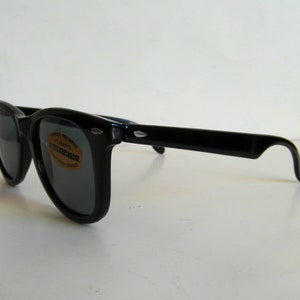 May include: Black plastic sunglasses with dark lenses. The sunglasses have a label on the right lens that says "Vesper Temples, Ultraviolet Absorbents, Polarized Lenses".